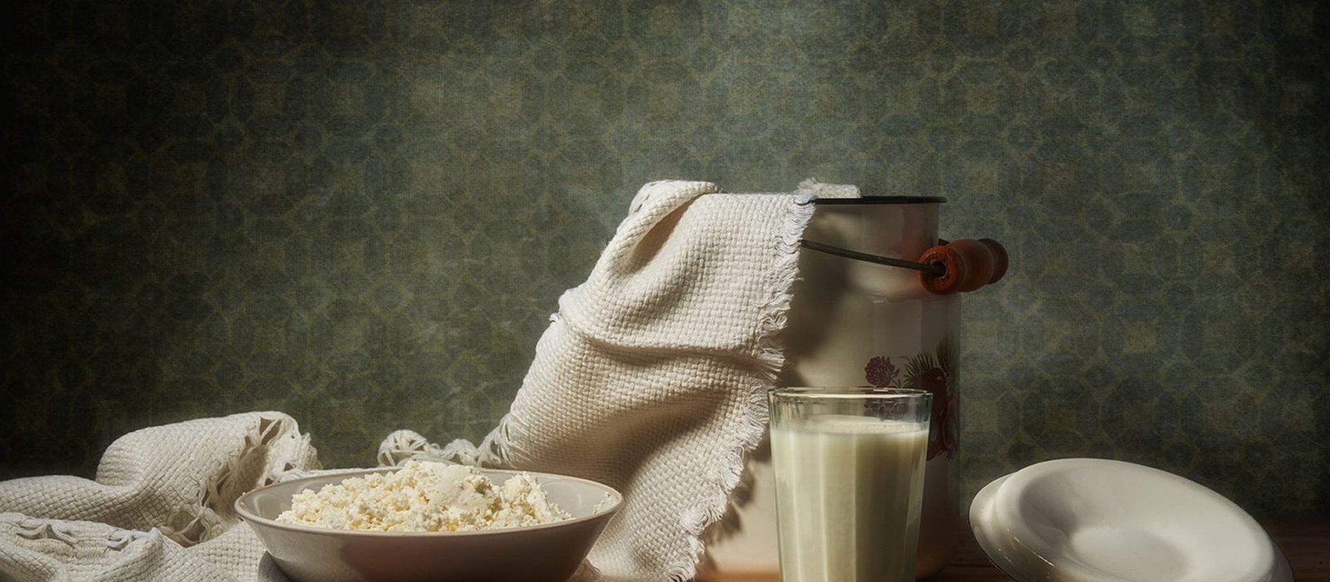 A bowl of curd, a jar of milk and linen on a dark wooden table