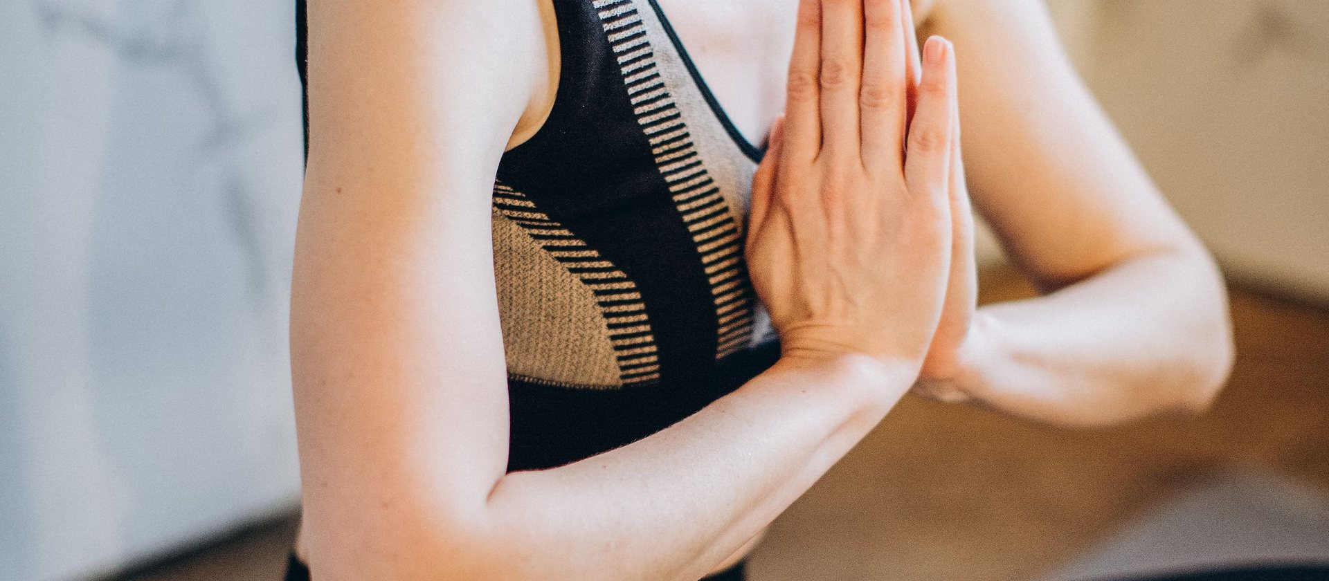 A woman seated with her palms joined at her chest in a calm, light room