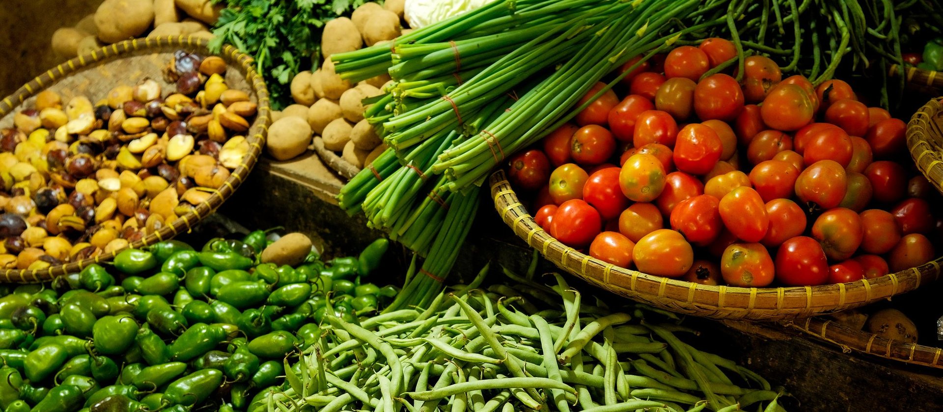 Baskets of fresh vegetables at a market — greens, beans, tomatoes and corn