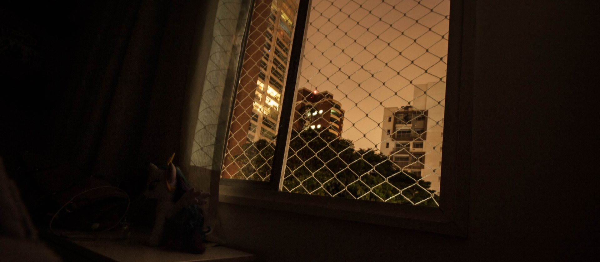 A dark bedroom at night with a city window lit beyond the sill